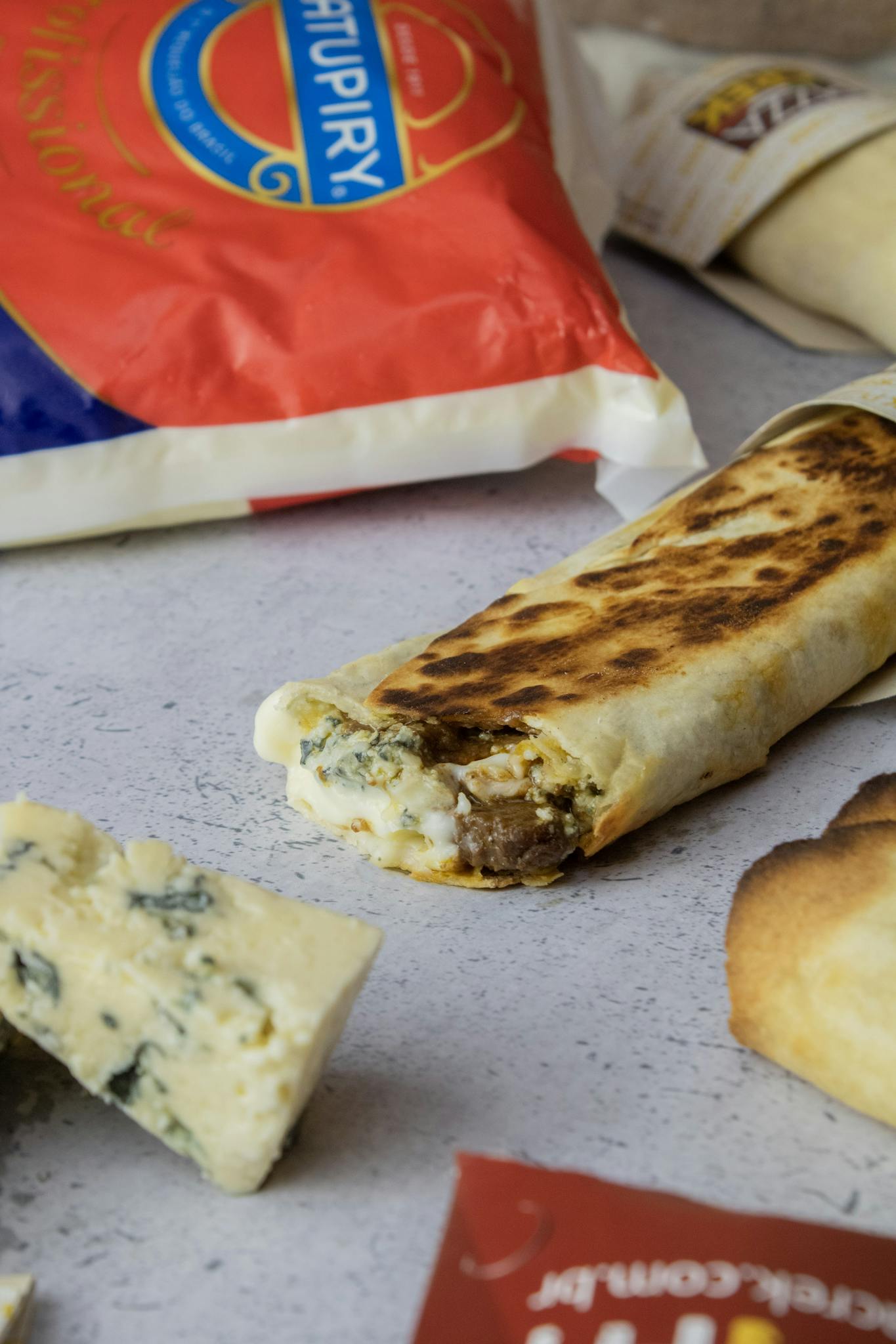 Close-up of a grilled doner roll surrounded by cheese and packaged ingredients.