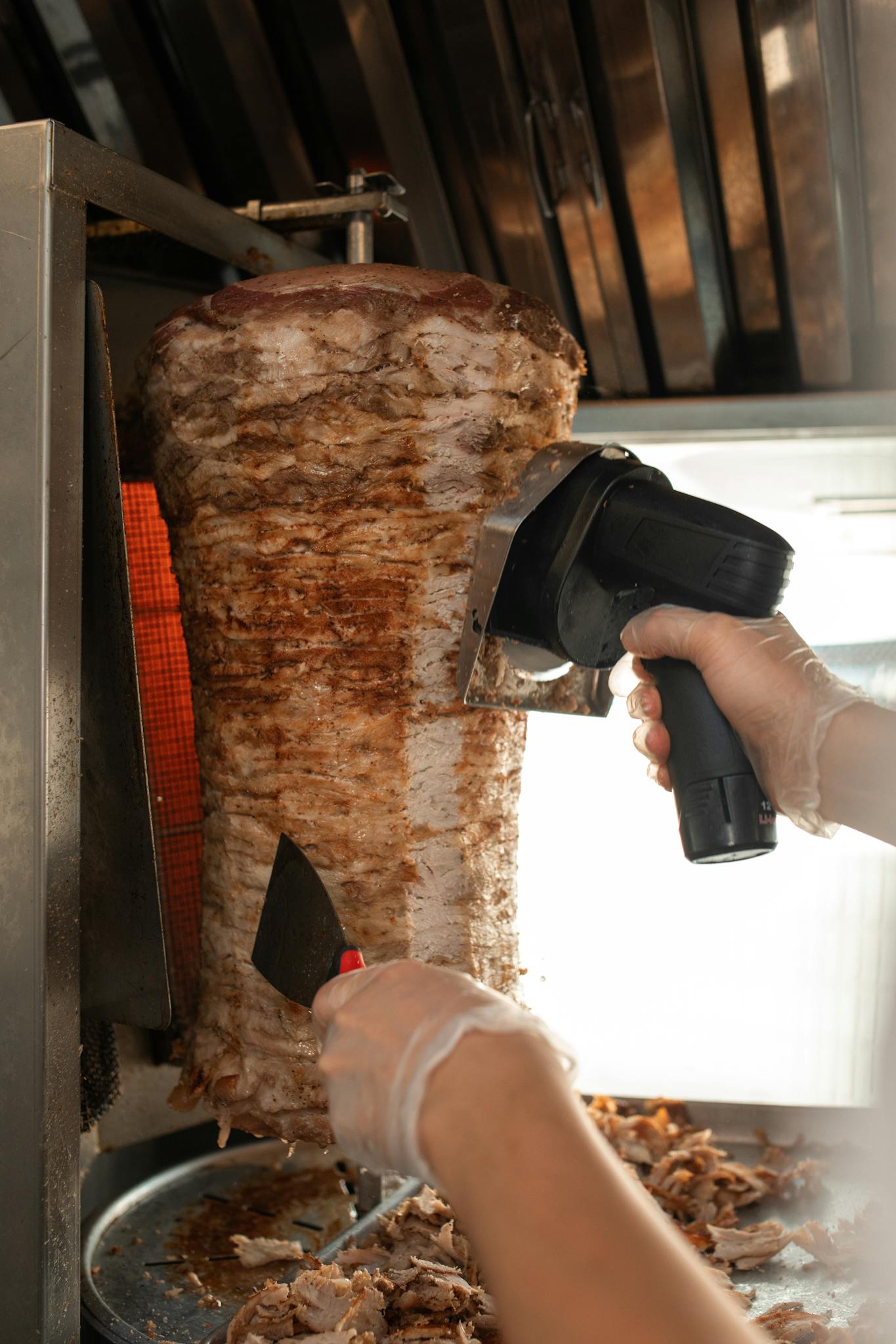 Close-up view of shawarma being sliced with professional equipment in a kitchen.